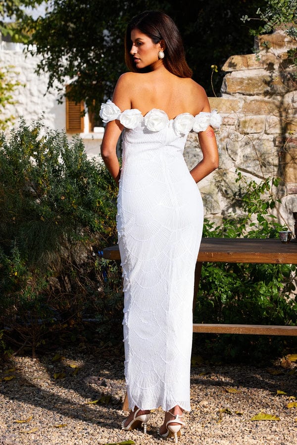 Vestido Fleur Blanche Vestido comprido branco com flores no ombro usado por mulher num jardim com vegetação e pedras
