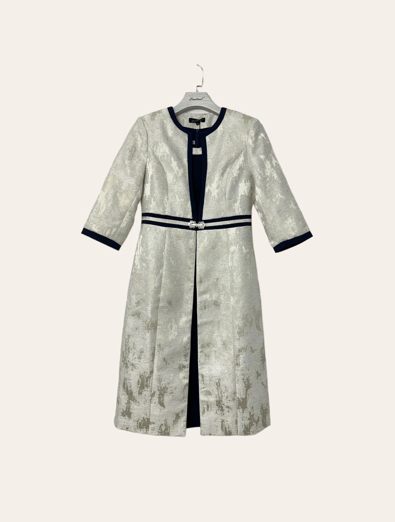 Conj. Lautinel (Blazer Comprido e Vestido) Casaco prateado com detalhes azul escuro e fecho prateado pendurado num cabide.