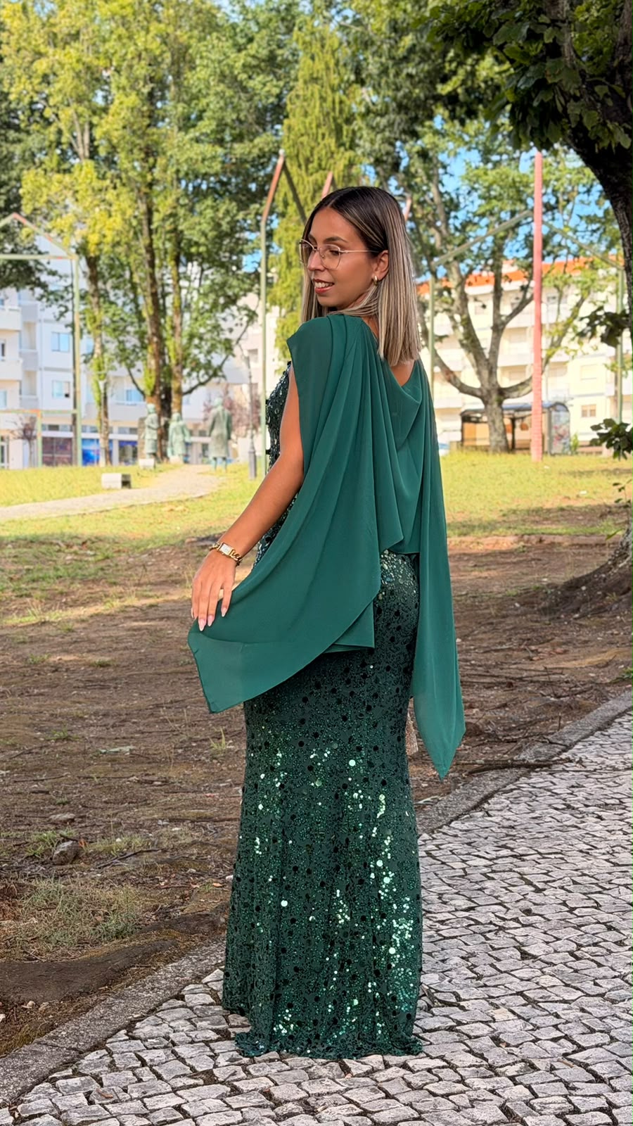 Vestido Milene Lantejoulas Mulher com vestido longo verde escuro com lantejoulas e capa fluida no parque