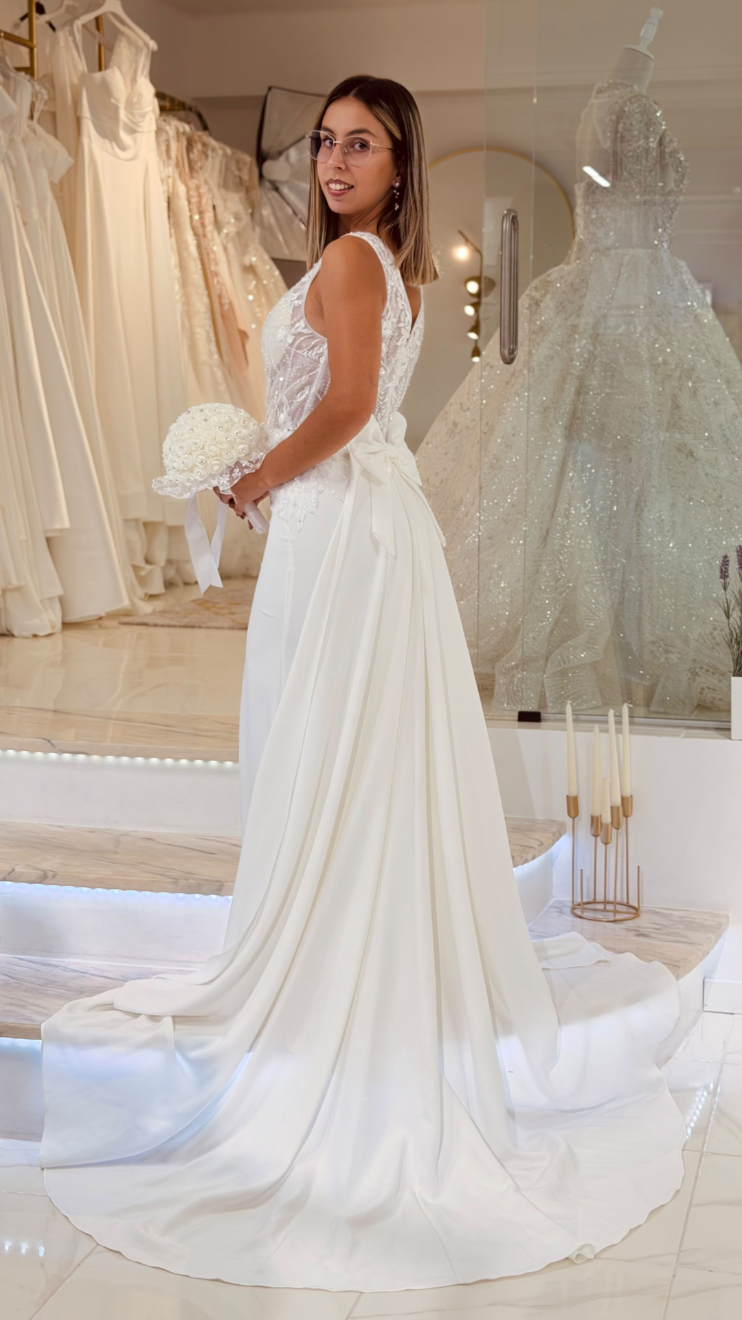 Vestido Denielle Noiva Mulher com vestido de noiva branco e bouquet em loja de vestidos.