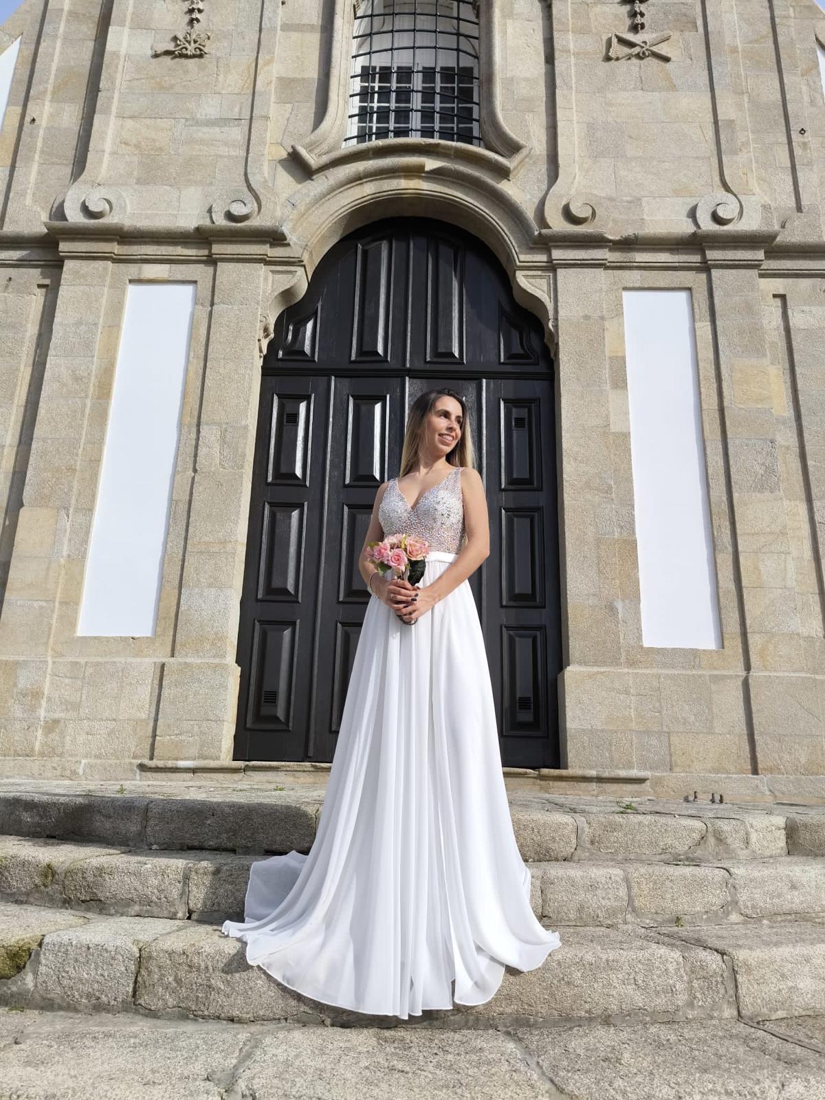 Vestido Simplicidade Serena Mulher com vestido de noiva branco em frente a porta grande preta de madeira e fachada de pedra