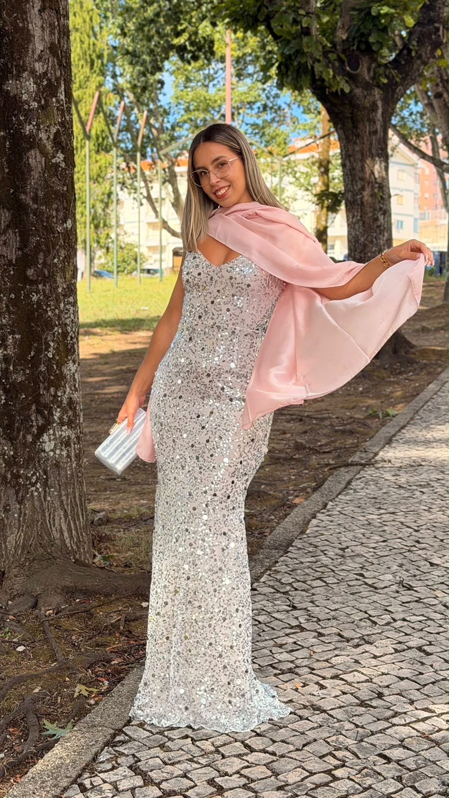 Vestido Milene Lantejoulas Mulher com vestido longo de lantejoulas prateadas e lenço rosa claro ao ar livre