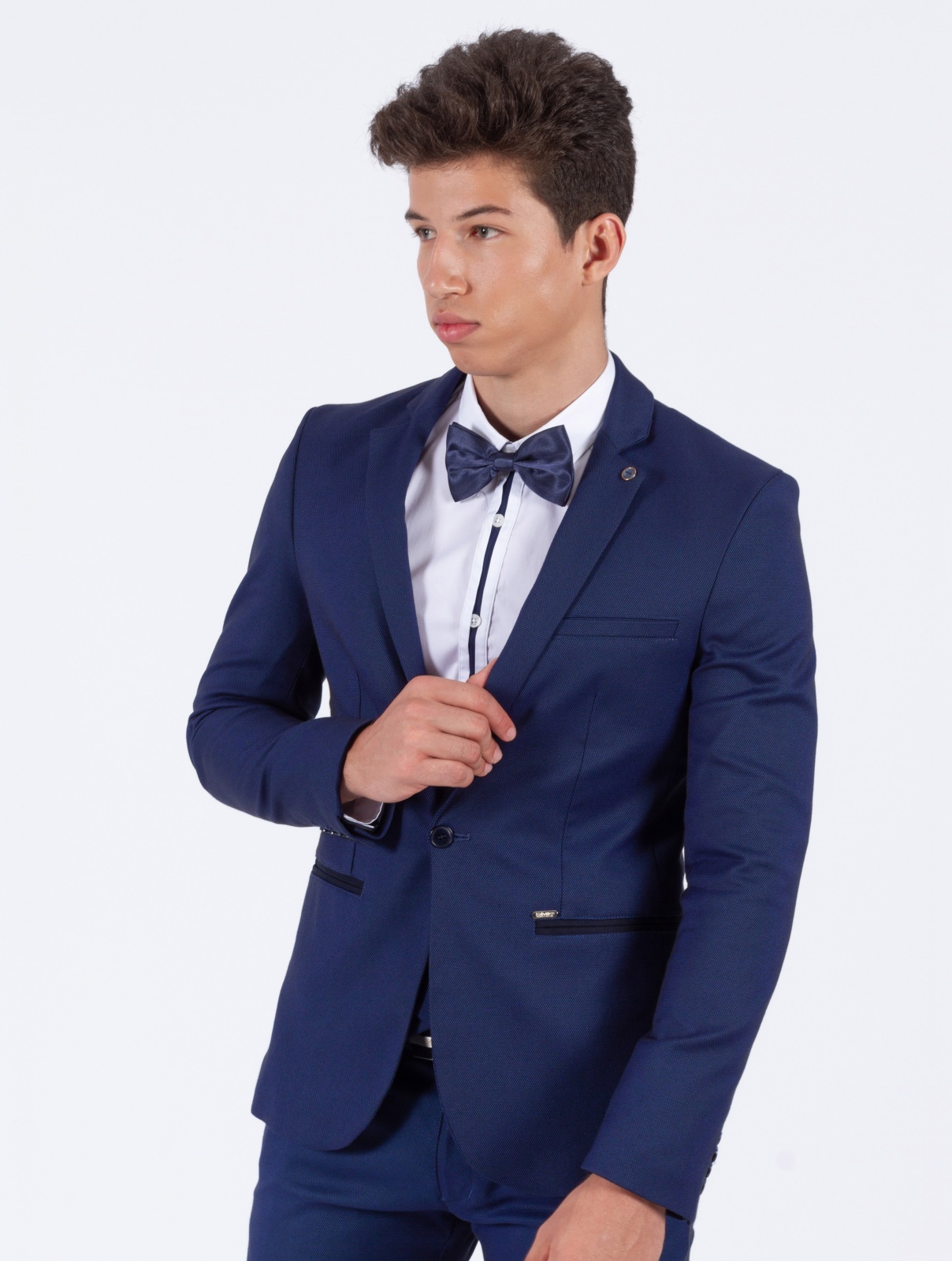 BLAZER SMK BLUE REFLECTIO Homem jovem com fato azul escuro, camisa branca e gravata borboleta azul
