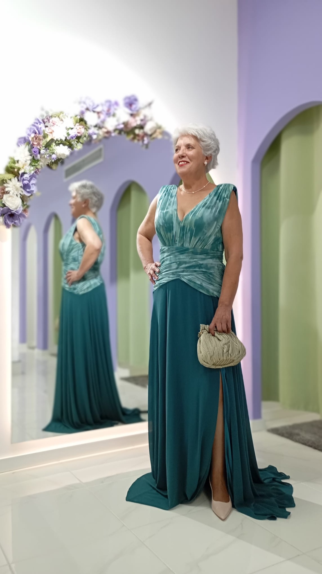 Vestido Andore Plus Size Senhora com vestido longo azul esverdeado em sala com espelho e flores.