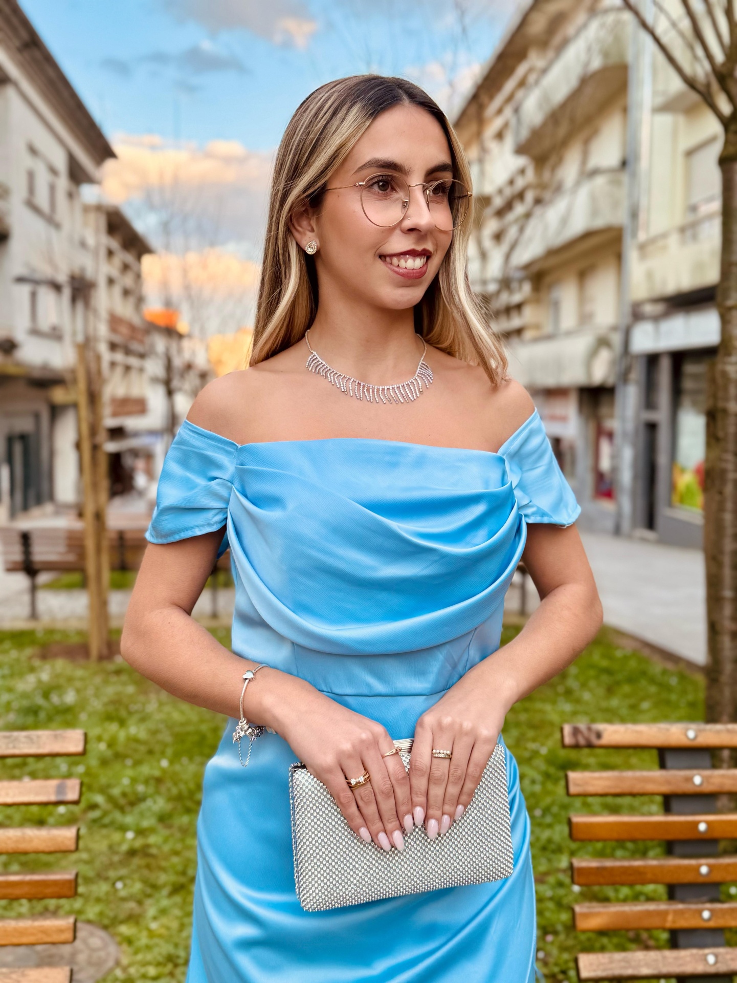 Vestido Sony Mulher com vestido azul claro acetinado e clutch prateada numa rua urbana