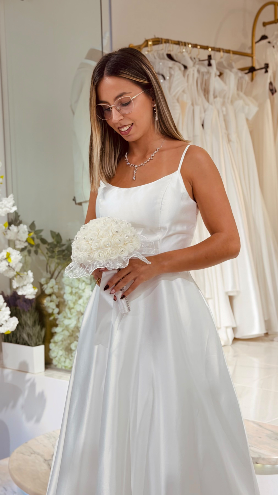 Vestido Helene Noiva Mulher com vestido de noiva branco acetinado e bouquet de rosas brancas em loja