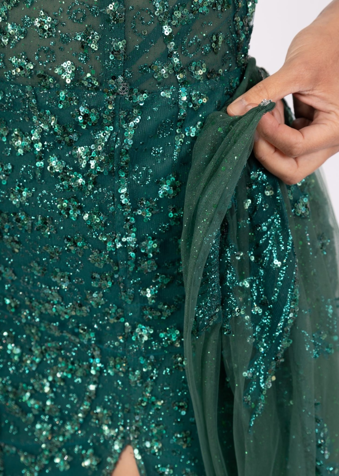 Vestido Raquel Brilho c/ Cauda Detalhe de vestido verde com lantejoulas e tule, mão segurando o tecido