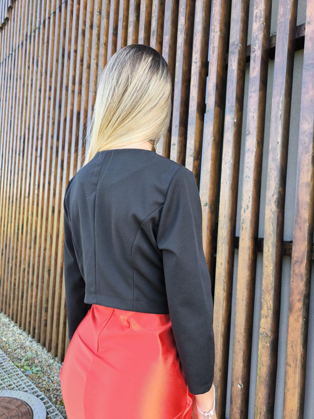 Bolero Simply Mulher com jaqueta preta e saia vermelha junto a grade metálica