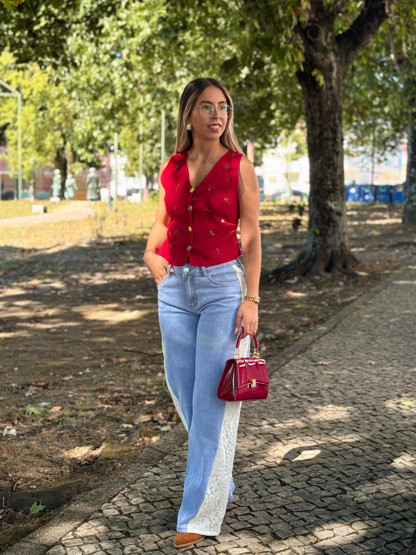 Calça de Ganga c/ Renda Branca Mulher com colete vermelho e calças de ganga bicolores numa calçada de parque