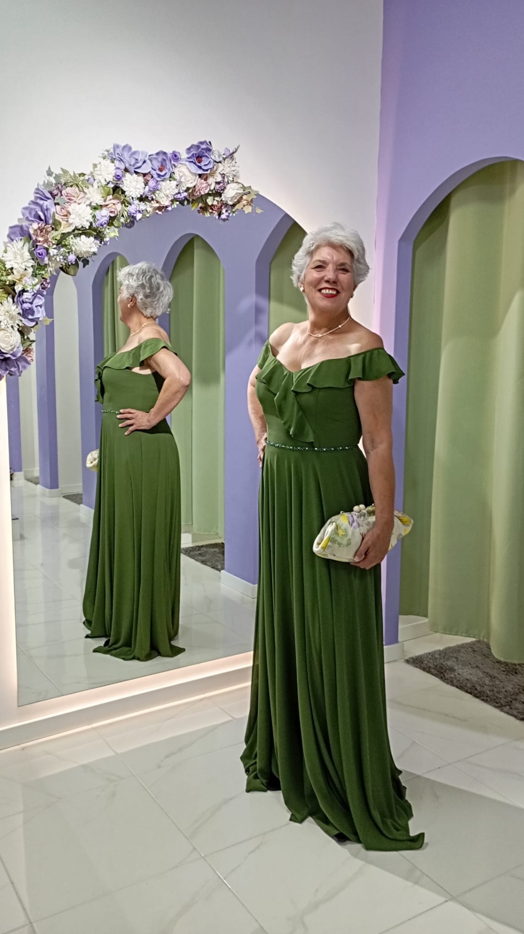 Vestido Nataly Mulher com vestido verde longo refletida em espelho com arco floral