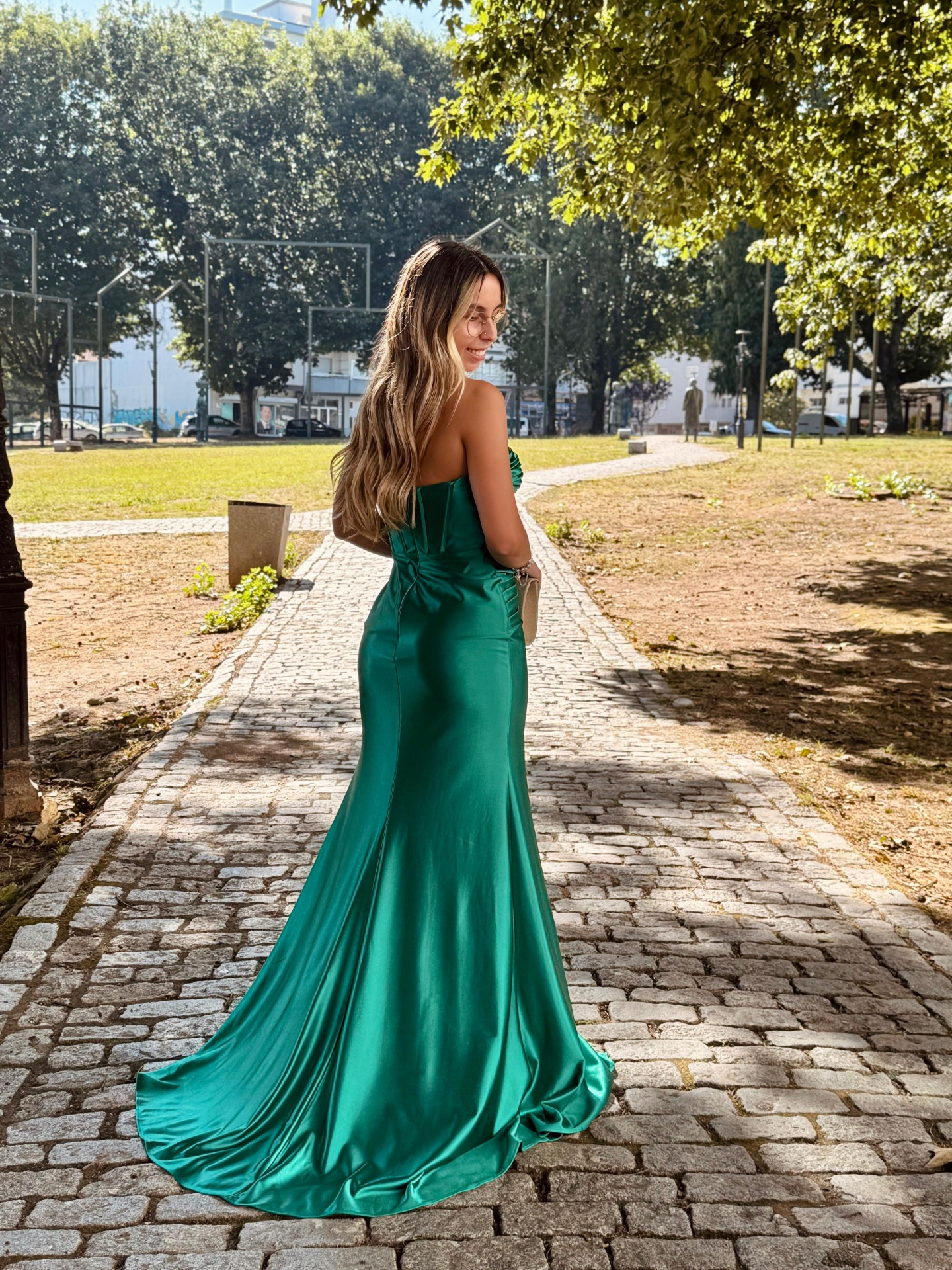 Vestido F&P Monique Mulher de costas usando vestido verde longo em pedra ao ar livre