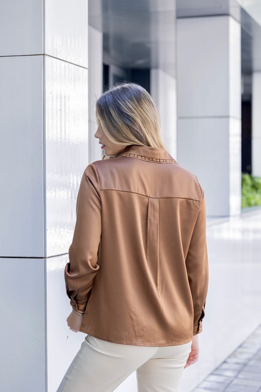 Blusa c/renda Moda Ana Mulher vista de costas com blusa castanha de manga comprida e calças brancas