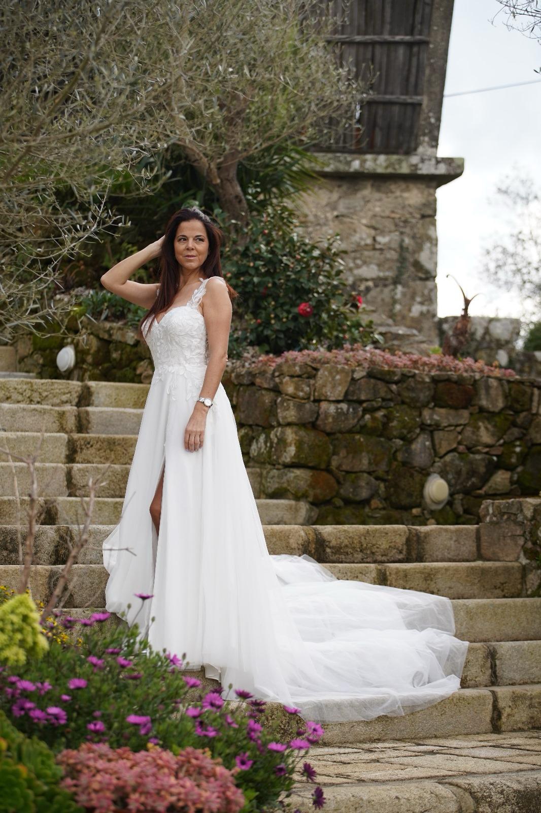 Vestido Amarílis Mulher com vestido de noiva branco longo com cauda numa escadaria de pedra exterior