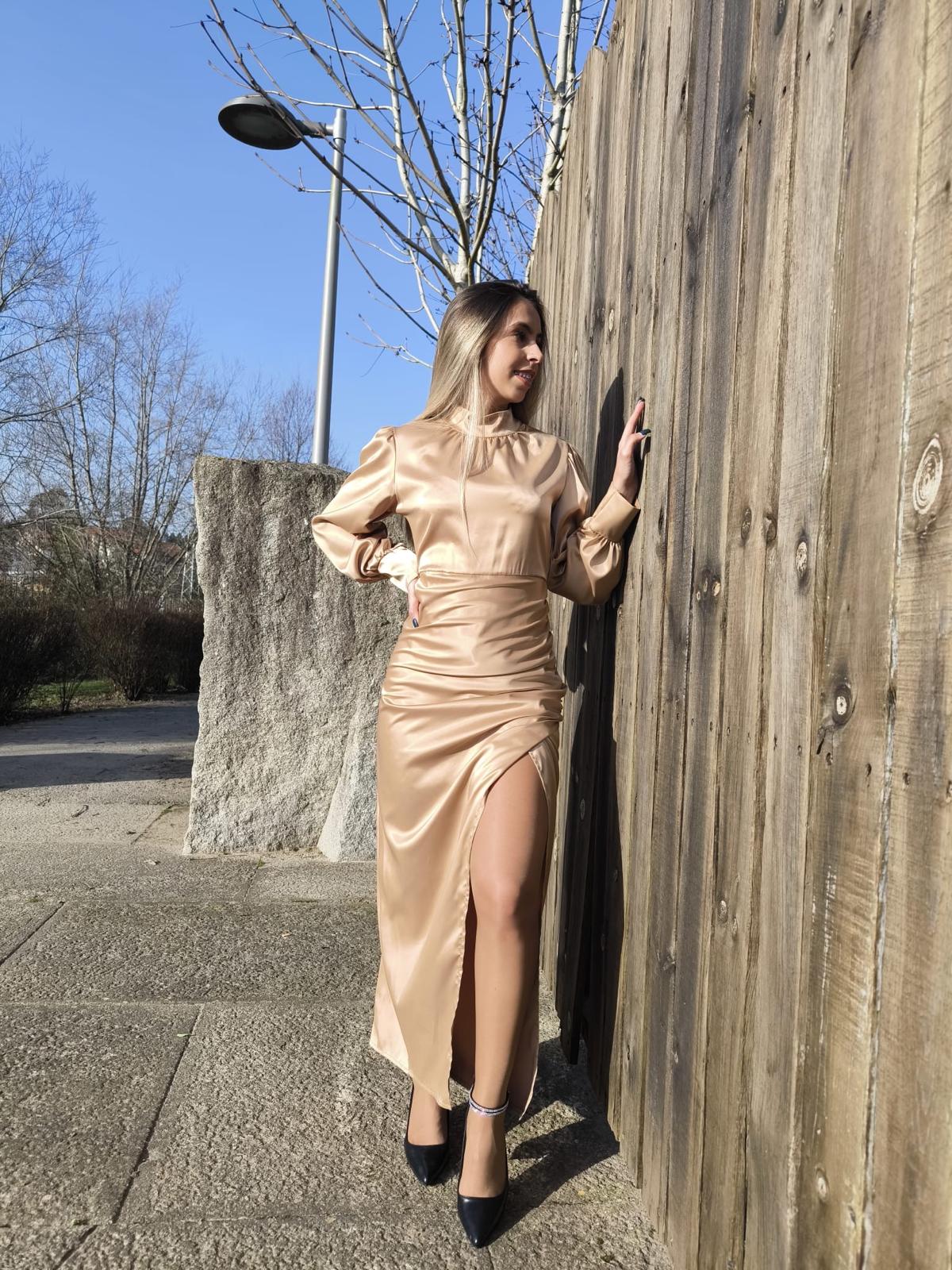 Vestido comprido c/ manga em cetim Mulher de vestido comprido dourado com fenda encostada a vedação de madeira