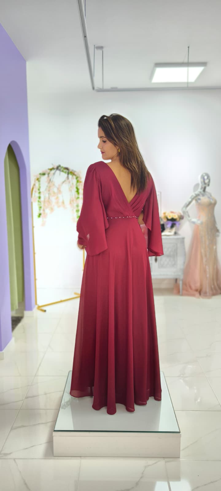 Vestido Leonor c/ Capa Plus Size Vestido longo bordô com mangas amplas e decote em V nas costas numa loja de roupa.