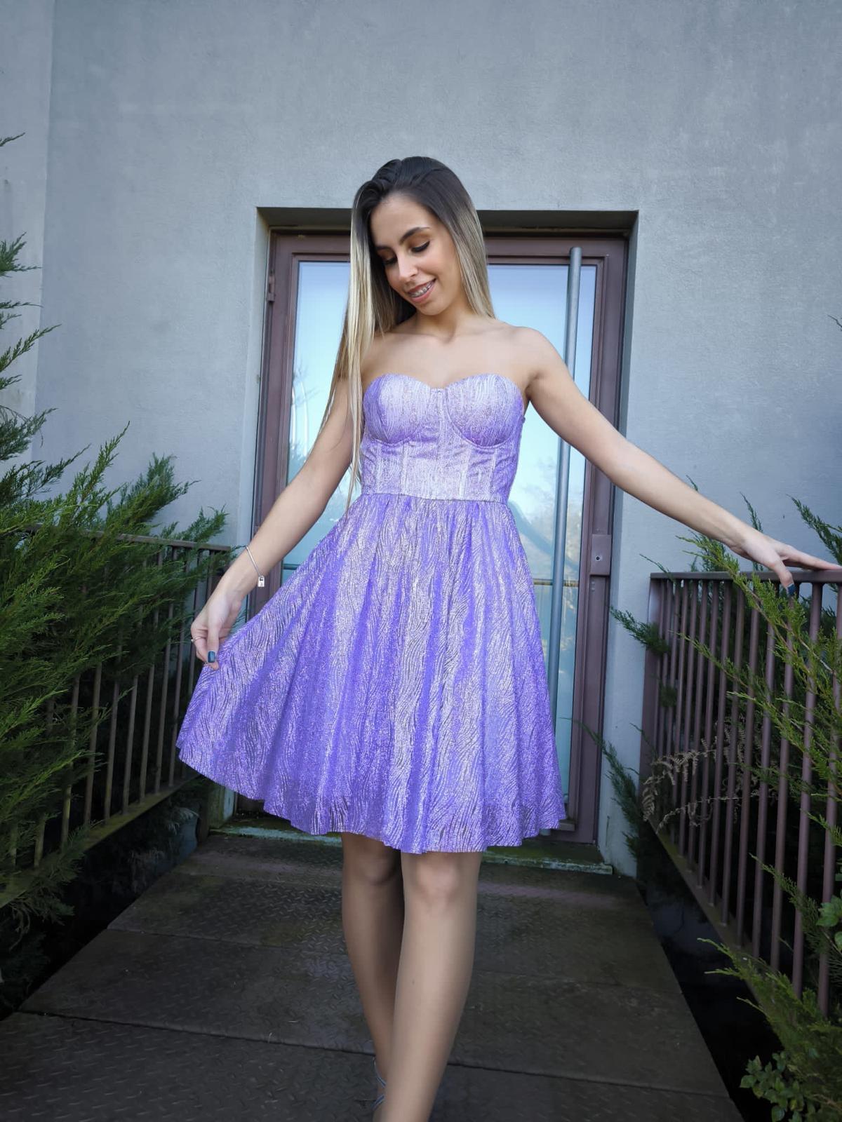 Vestido Glam Princess Mulher com vestido lilás brilhante sem alças em ambiente exterior com portão e arbustos