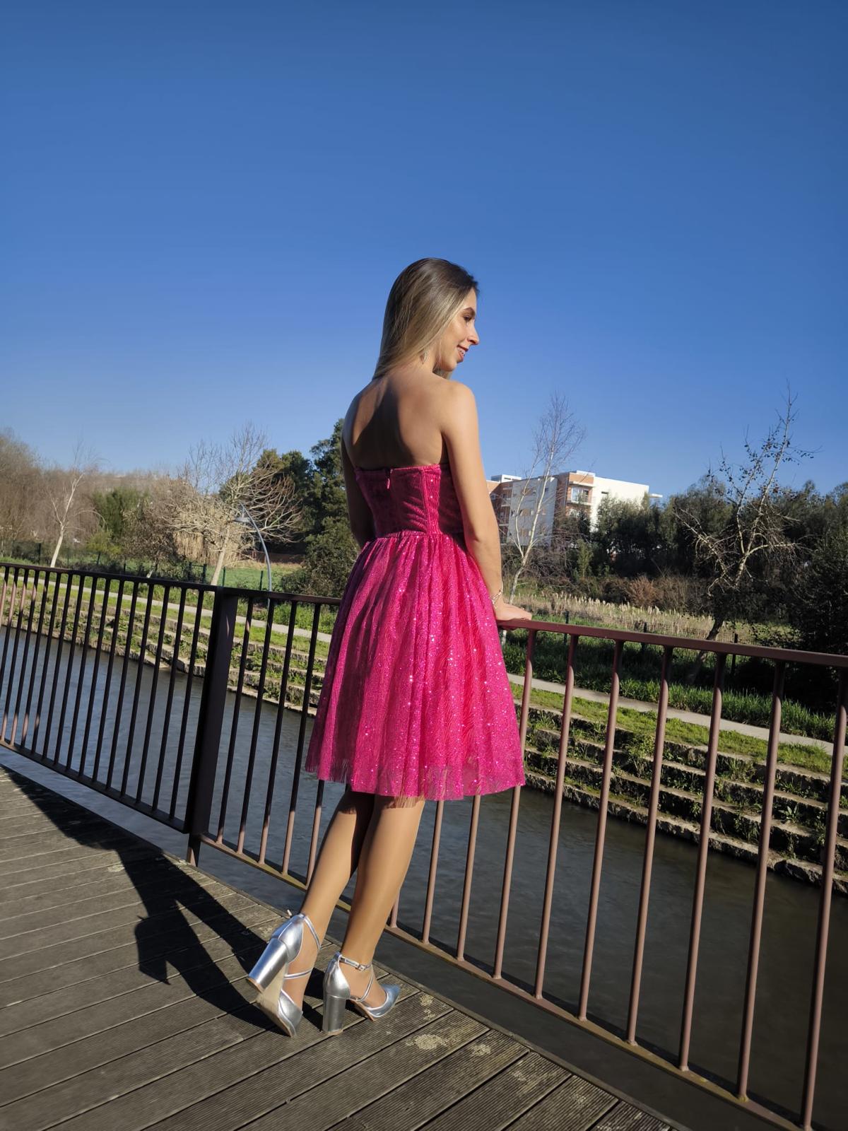 Vestido Glam Princess Mulher de vestido rosa cintilante e sapatos prateados num passadiço à beira de rio