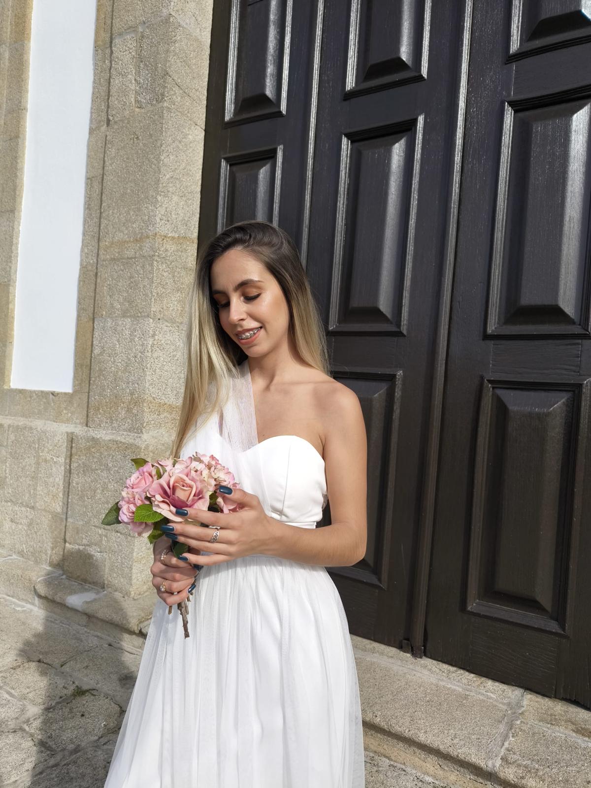 Elegância Minimalista - Vestido Noiva Mulher com vestido de noiva branco e bouquet de flores junto a uma porta de madeira escura