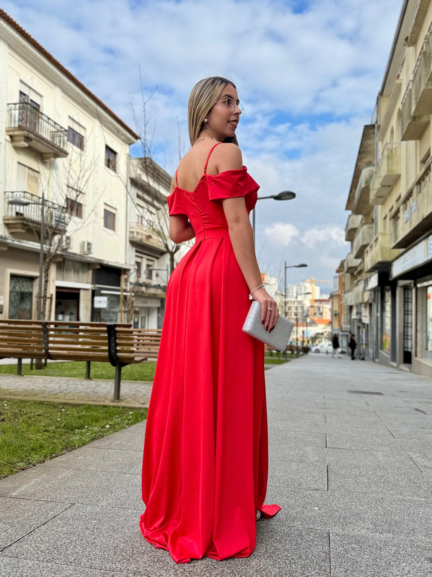 Vestido Eleganza Mulher de vestido comprido vermelho com alças finas e folhos nos ombros numa calçada urbana