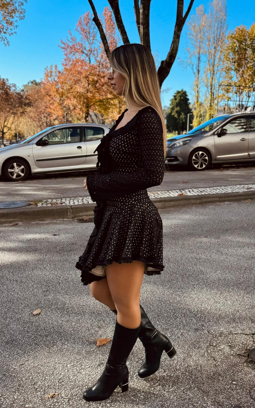 Vestido Tricot Charm Mulher com vestido preto de pontos brancos e botas pretas numa rua com carros e árvores
