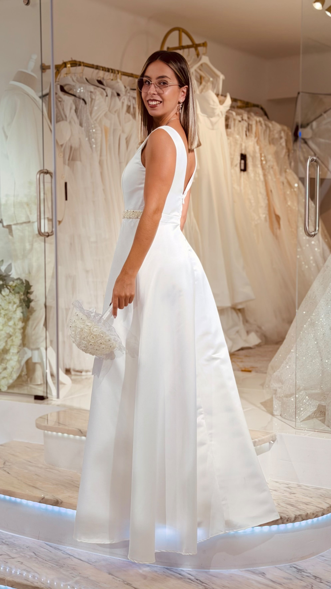Vestido Glace Noiva Mulher de vestido branco de noiva com cinto de pérolas e bouquet na mão numa loja de vestidos de noiva