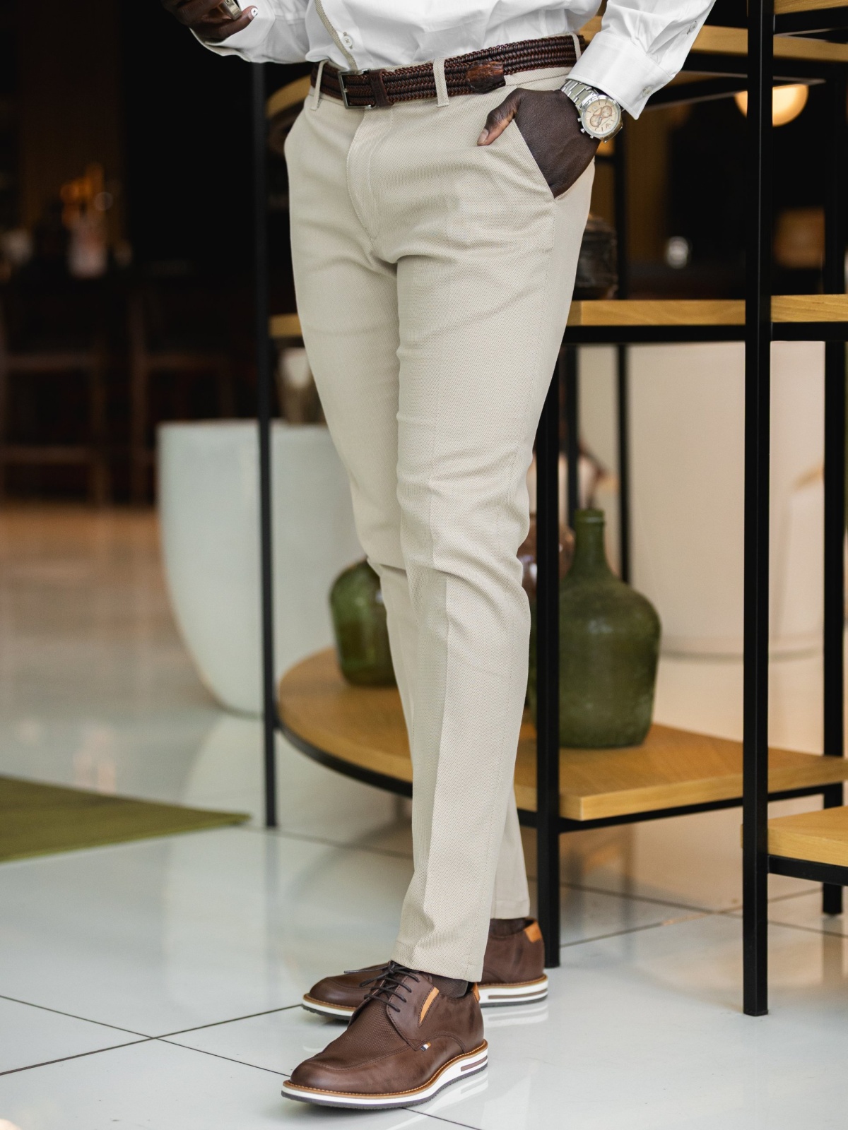 Calça SMK Golden Wear Calças bege com cinto castanho, camisa branca e sapatos castanhos em ambiente interior com móvel decorativo
