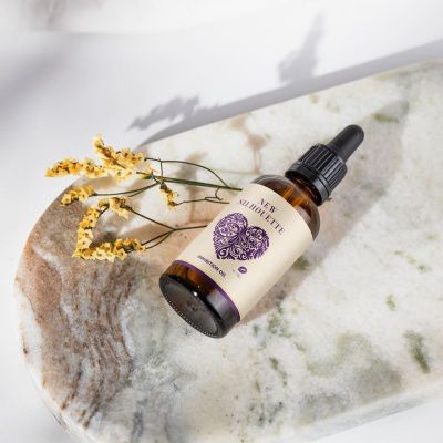 Inhibition Oil Frasco âmbar com conta-gotas sobre bloco de mármore e flores amarelas secas