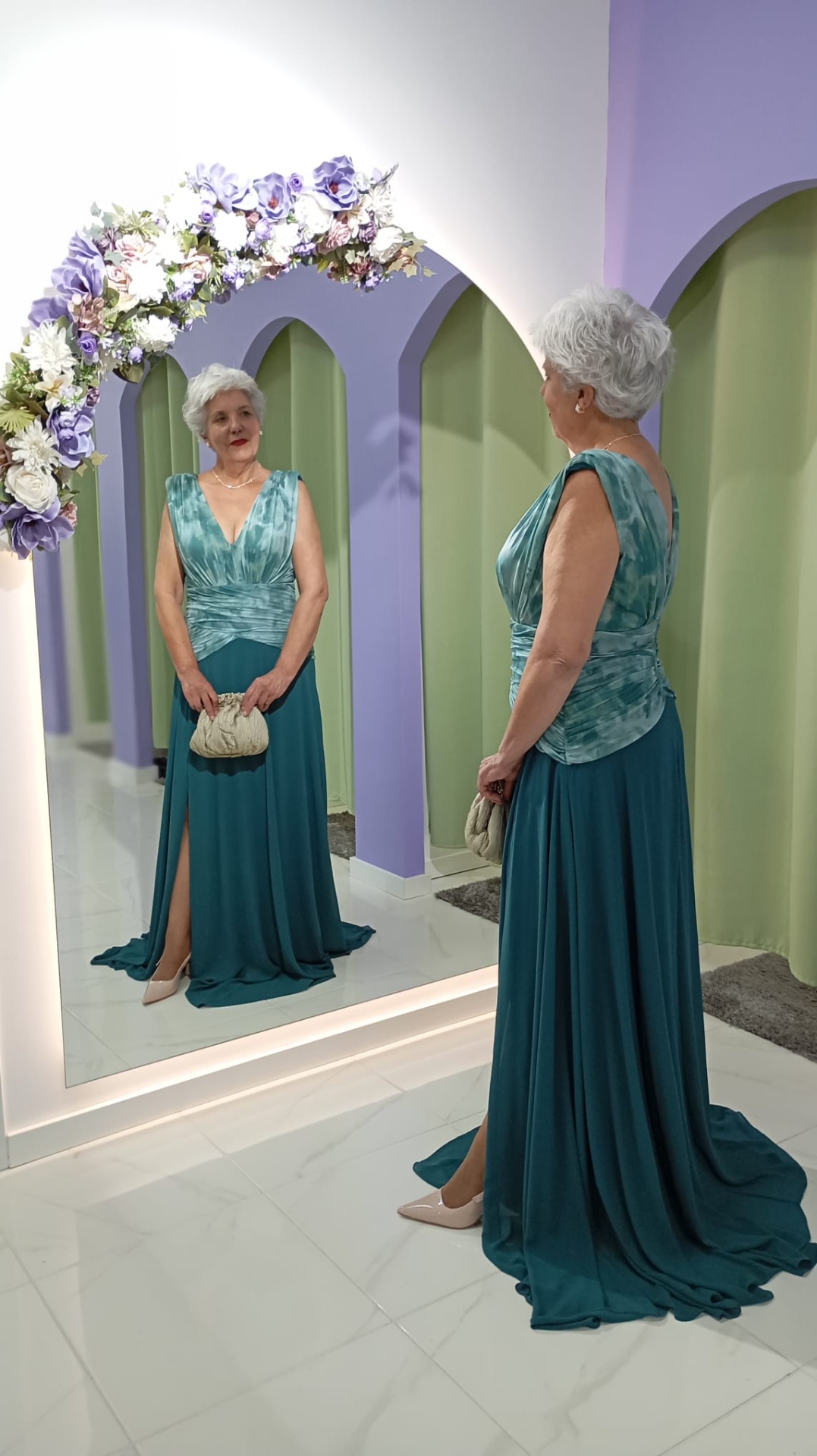 Vestido Andore Plus Size Mulher com vestido longo azul esverdeado a olhar para espelho grande com moldura florida