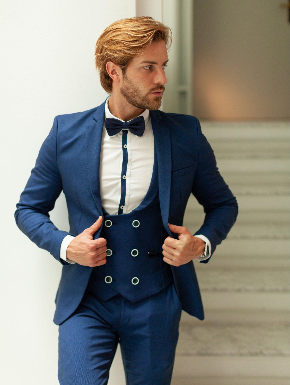 BLAZER SMK BLUE REFLECTIO Homem com fato azul e gravata borboleta em escadaria interior