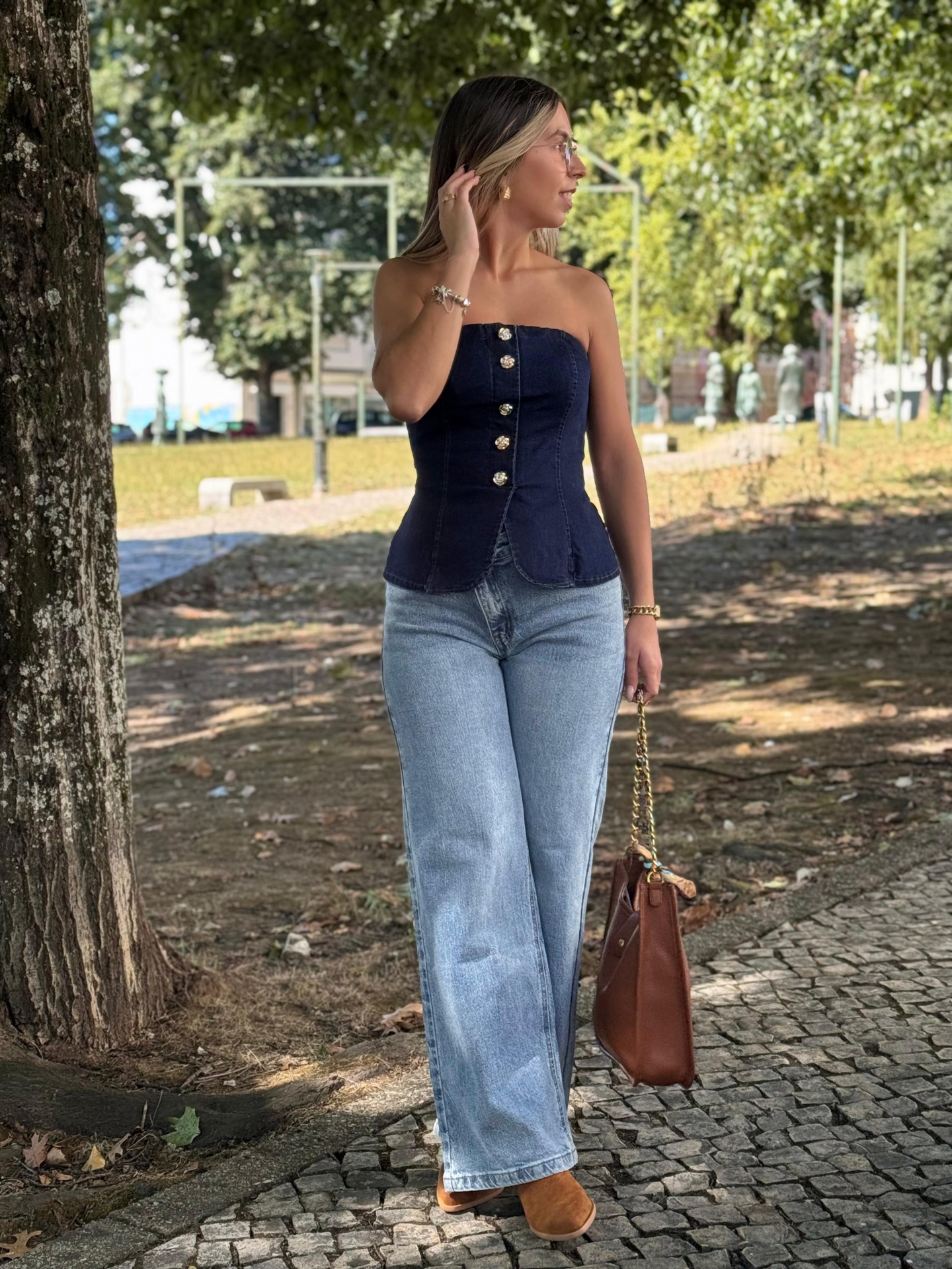 Calça de Ganga Foly Mulher com colete azul escuro, jeans largos e bolsa castanha ao ar livre