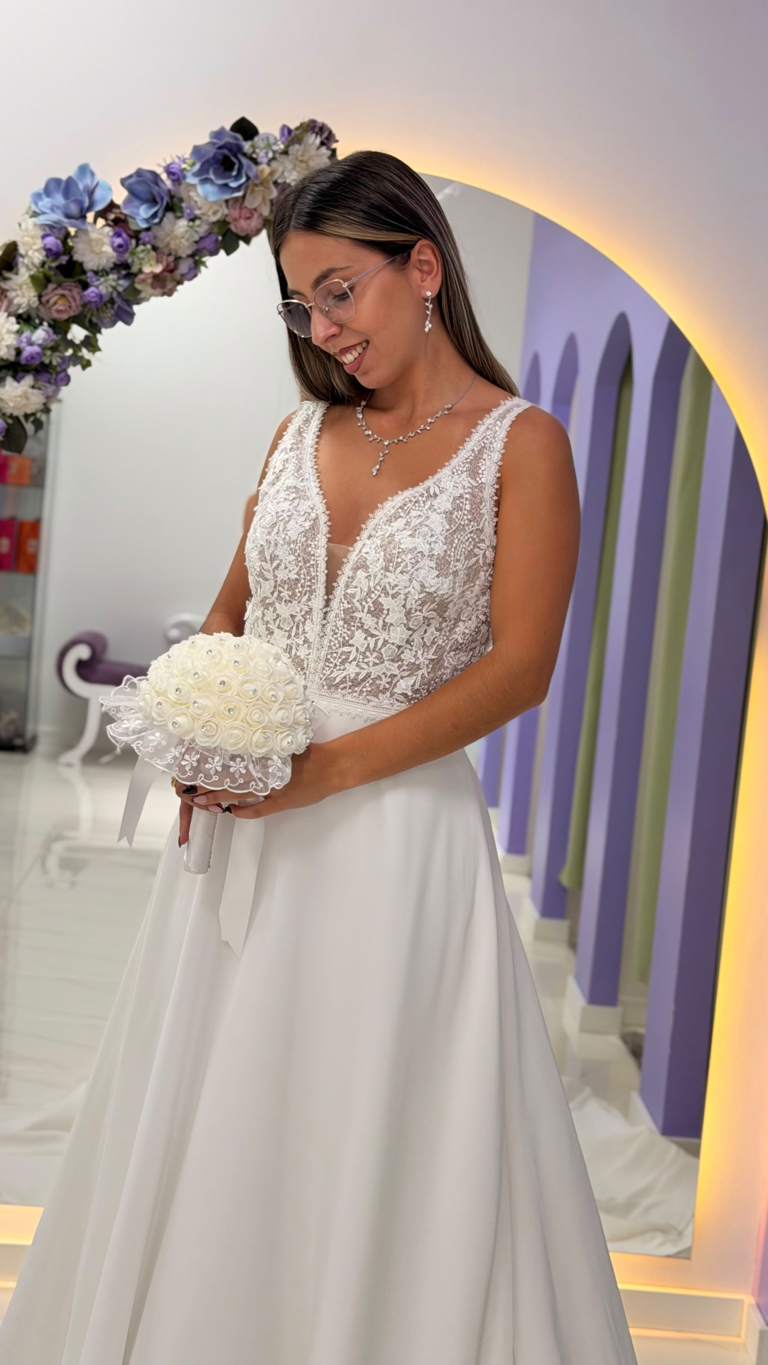 Vestido Miriam Noiva Mulher de vestido de noiva branco com corpete em renda com bouquet branco em estúdio decorado.