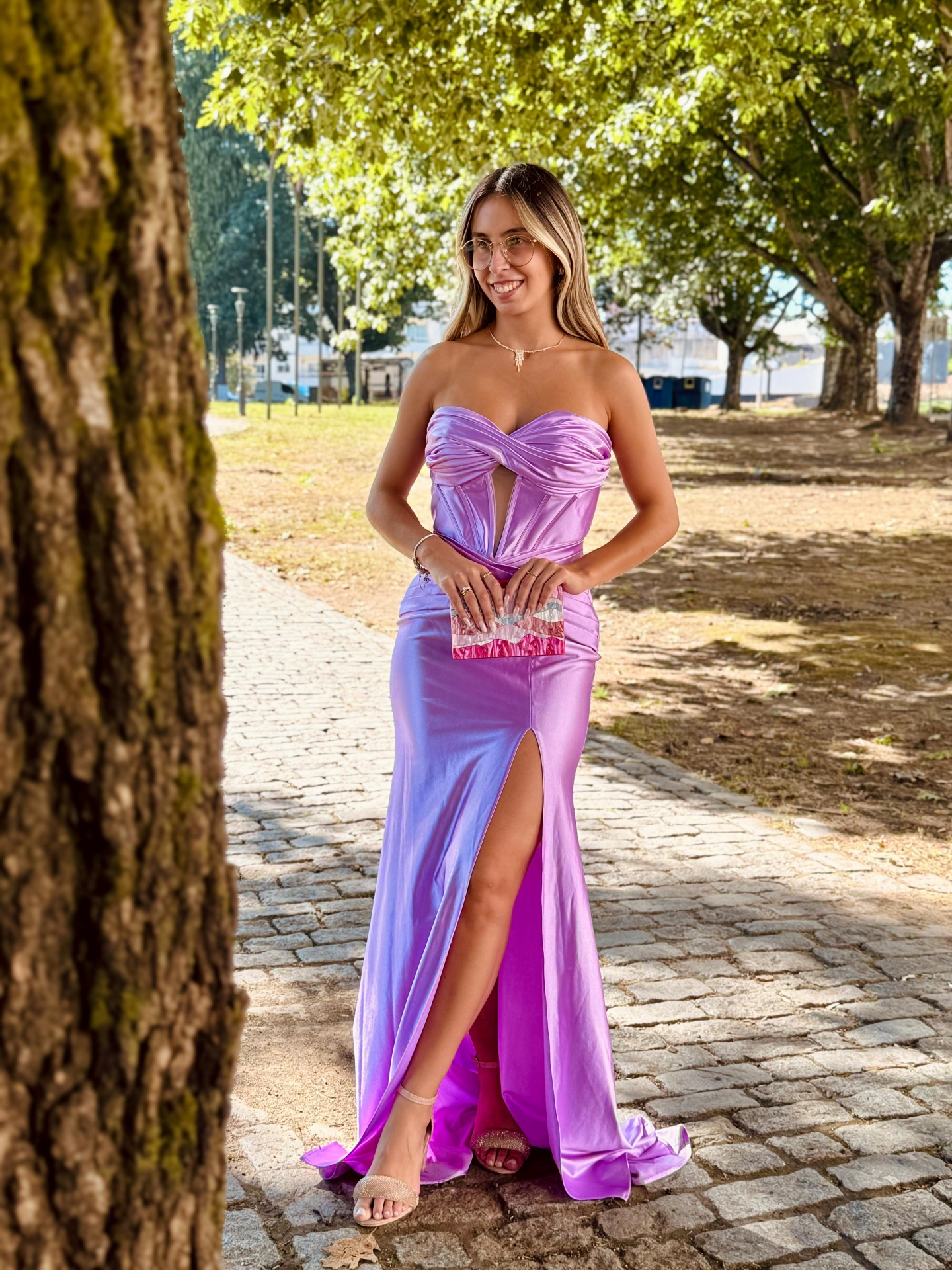 Vestido F&P Monique Mulher com vestido lilás longo com fenda lateral e mala rosa ao ar livre