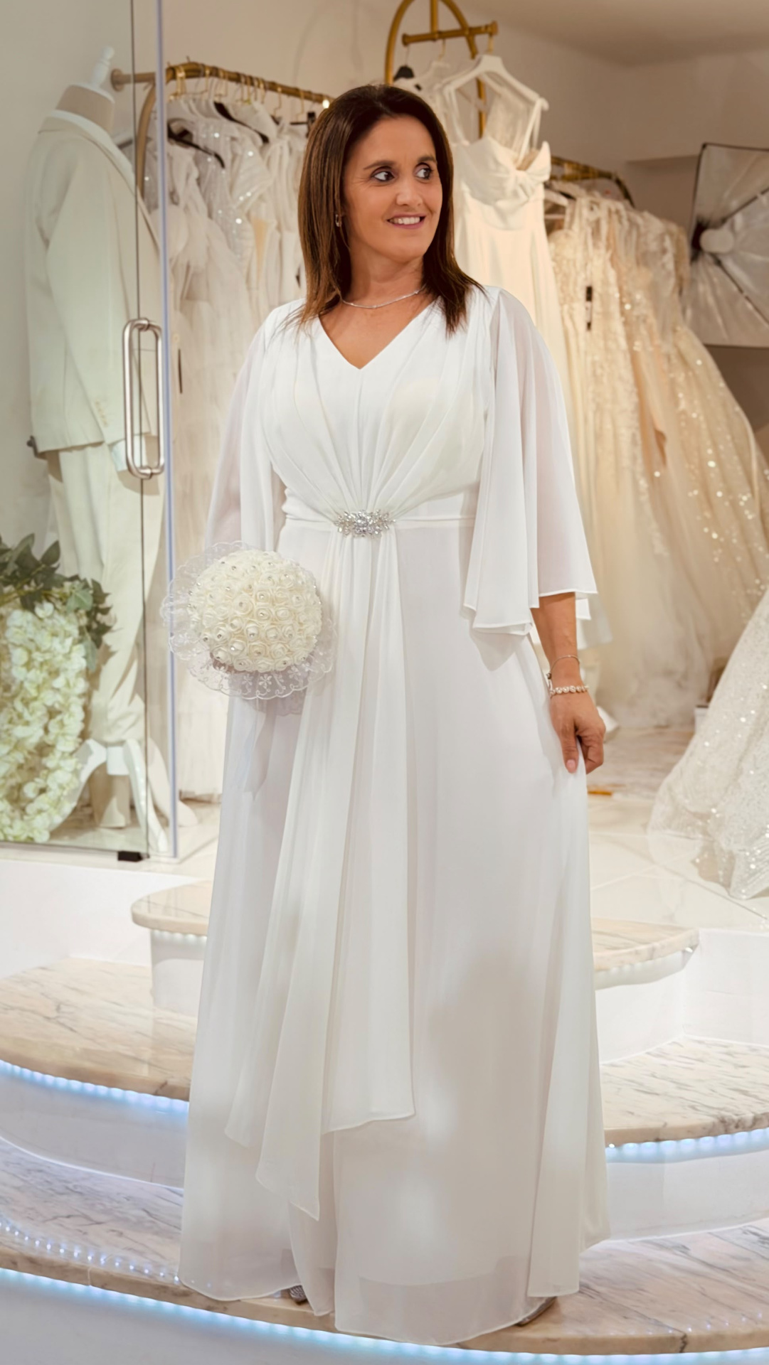 Vestido Rosário Noiva Mulher com vestido de noiva branco em loja de vestidos com floreira branca