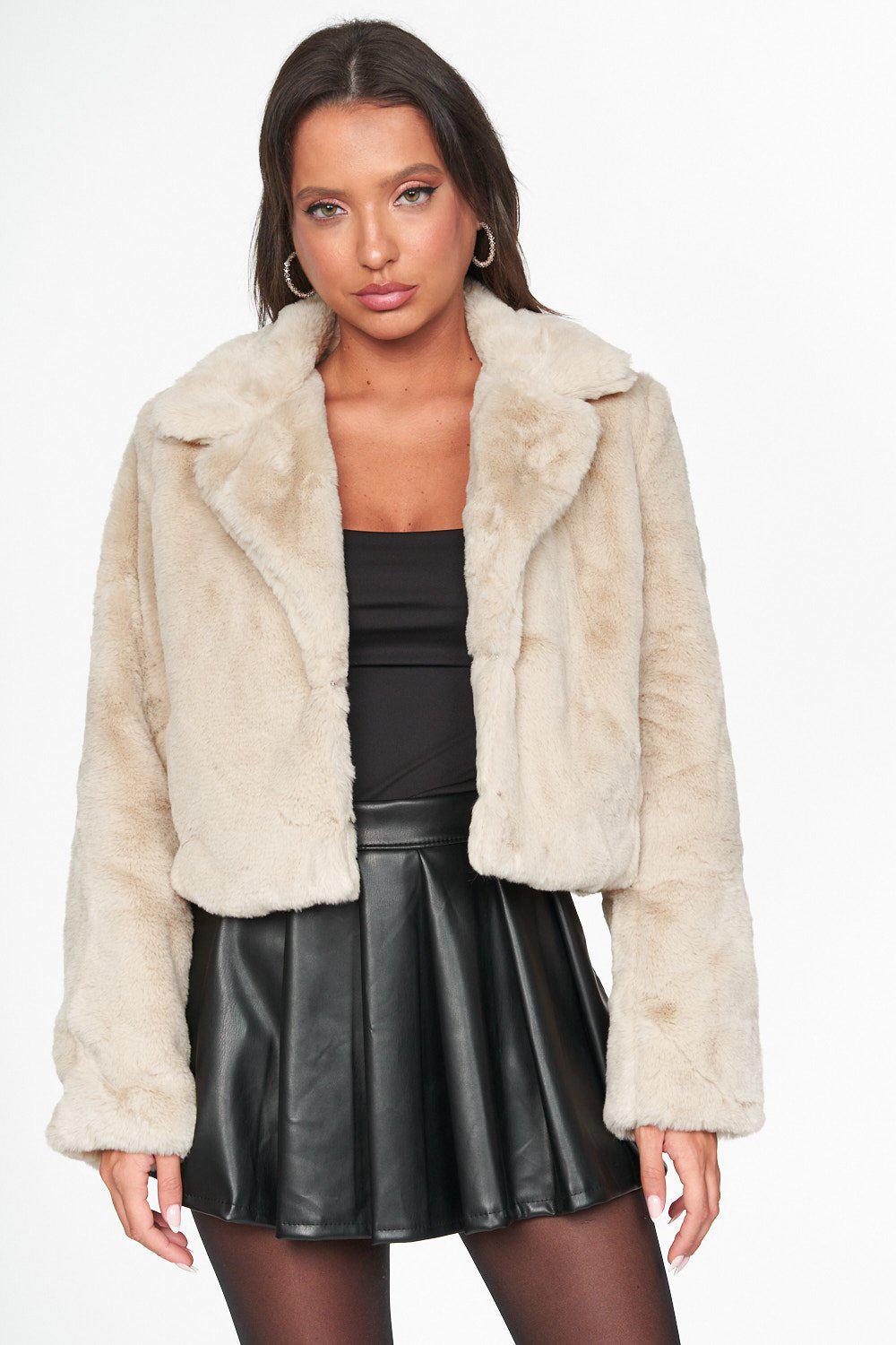 Bolero de pêlo Mulher a usar casaco curto bege de pelo sintético com gola grande e saia preta de pele.