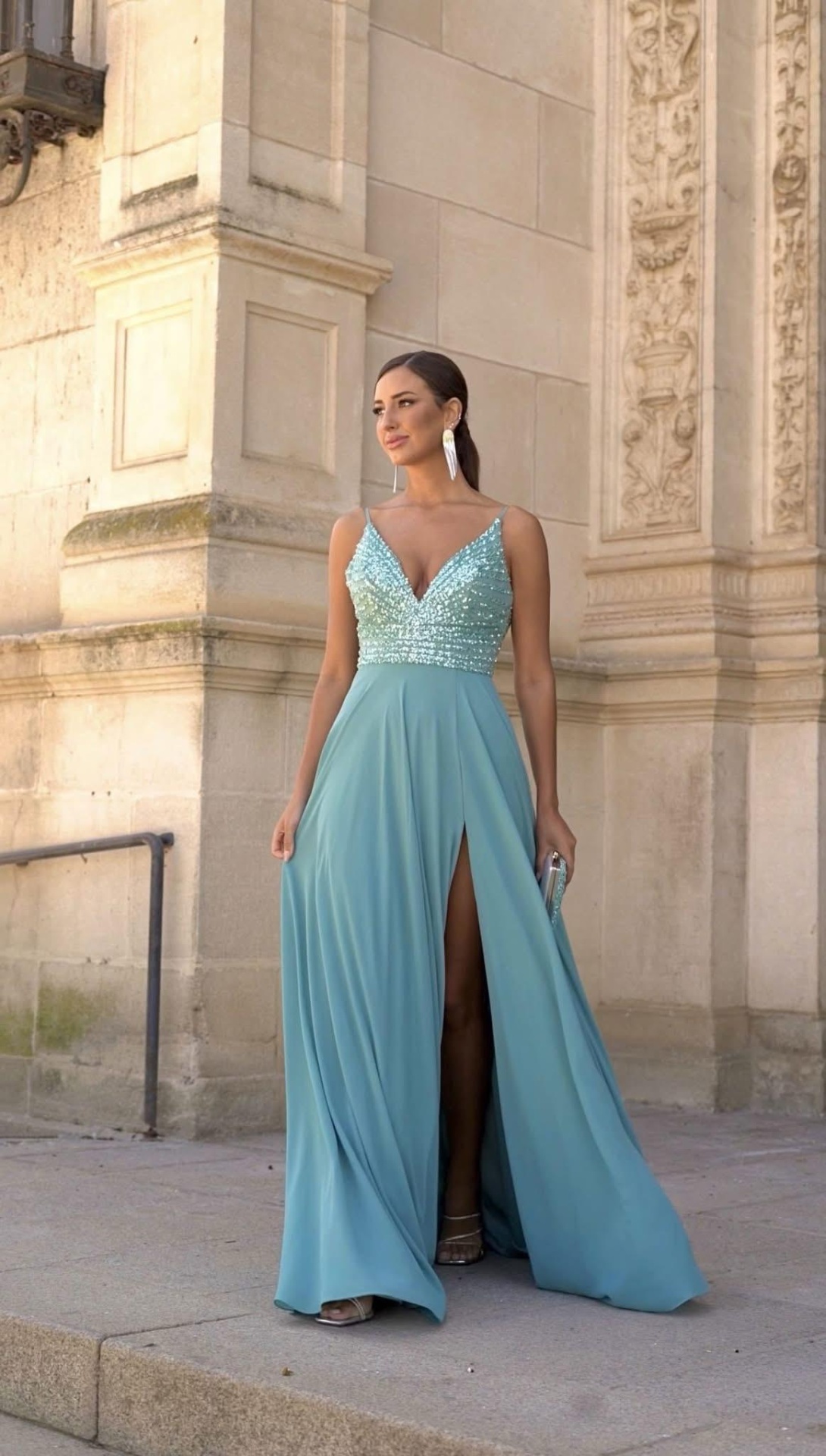 Vestido Isabela Mulher usando vestido longo azul claro com corpete bordado e saia com racha, parede de pedra ao fundo