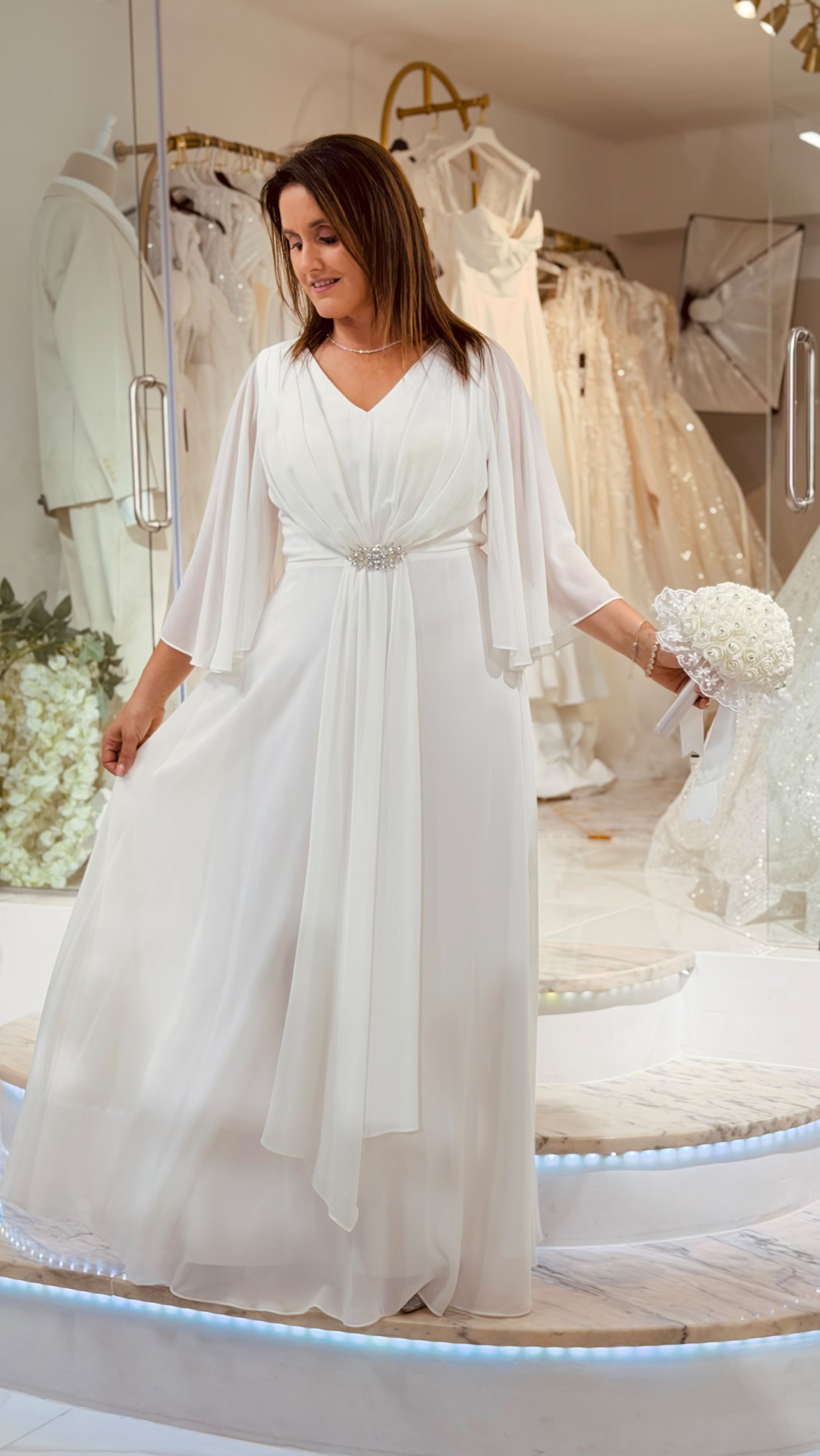 Vestido Rosário Noiva Mulher com vestido de noiva branco e bouquet em loja de vestidos.