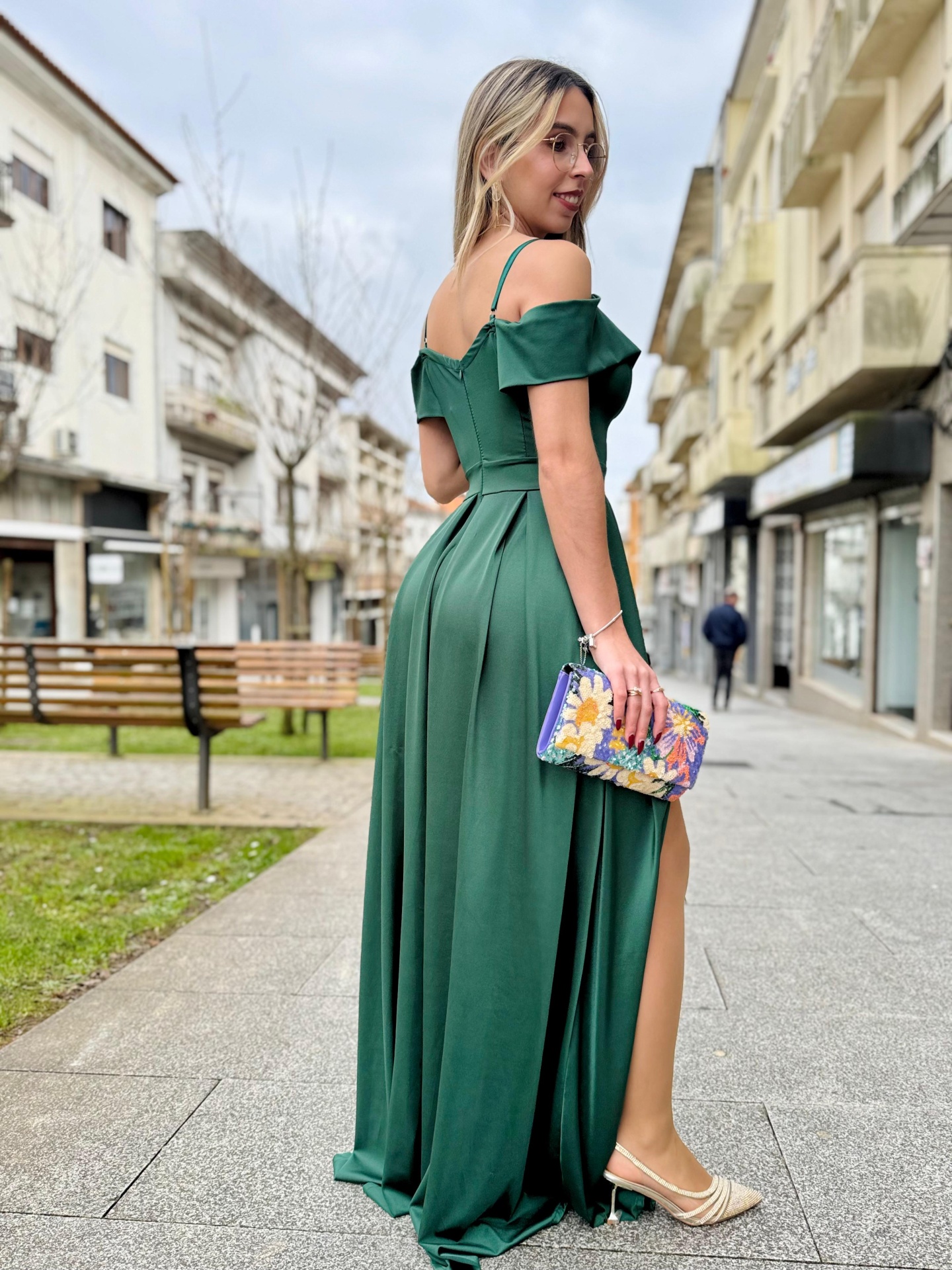 Vestido Eleganza Mulher de vestido longo verde escuro com carteira floral numa rua urbana