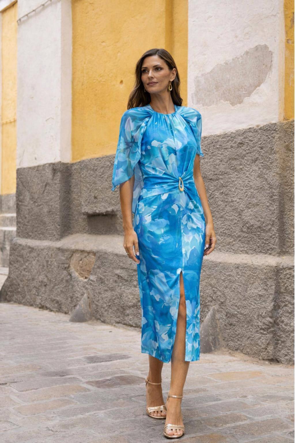 Vestido Dolcezza Petals Mulher a usar vestido midi azul floral com fenda e cinto, sandálias douradas, numa rua de pedra