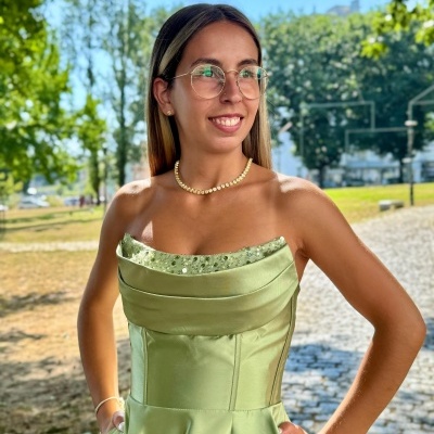 Vestido verde de seda brilhante com detalhes em paetês usado por mulher com colar de pérolas e óculos, ao ar livre