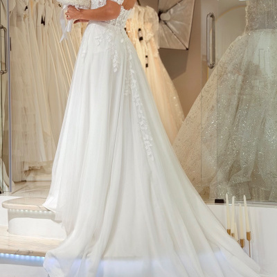 Vestido de noiva branco com renda floral e saia ampla, mulher a segurar bouquet branco em loja