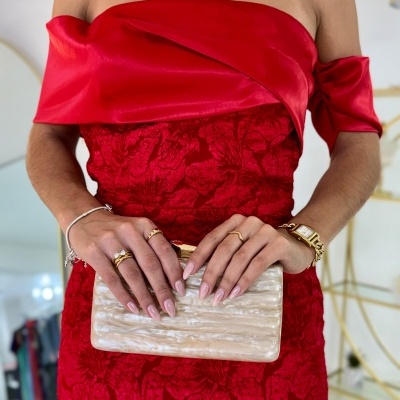 Vestido vermelho floral com mangas curtas e carteira bege perolada nas mãos