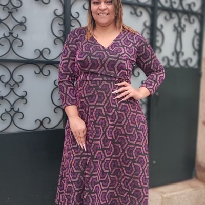 Vestido comprido estampado em tons roxos com sapatos pretos e portão de ferro ao fundo