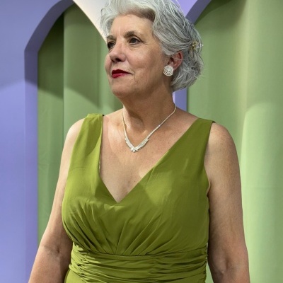 Mulher com vestido verde musgo e joias em fundo colorido com arcos.