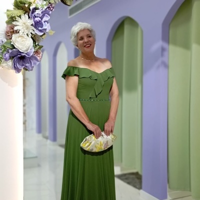 Mulher com vestido verde posando em arco floral em ambiente com paredes lilás