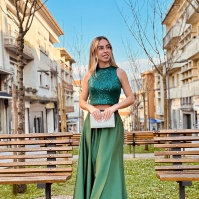 Mulher loira com vestido de festa verde em ambiente urbano com bancos de madeira