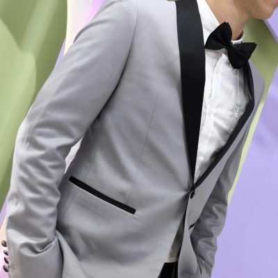 Fato masculino cinzento com lapela preta e laço preto em ambiente lilás e verde com flores