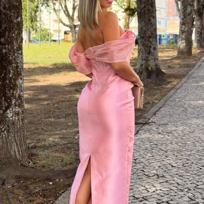 Mulher com vestido longo rosa e salto alto branco num passeio ao ar livre com árvores.