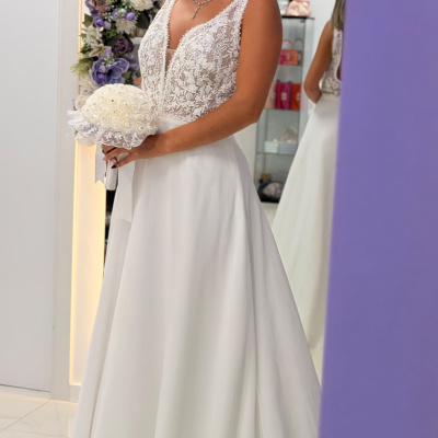 Mulher com vestido de noiva branco e buquê, arco floral ao fundo