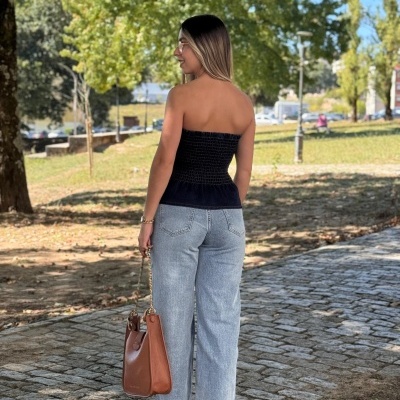 Mulher com top preto, jeans cinza e bolsa castanha ao ar livre num passeio