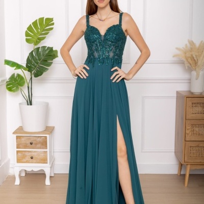 Vestido verde-azulado bordado com fenda lateral e sandálias prateadas num ambiente interior minimalista